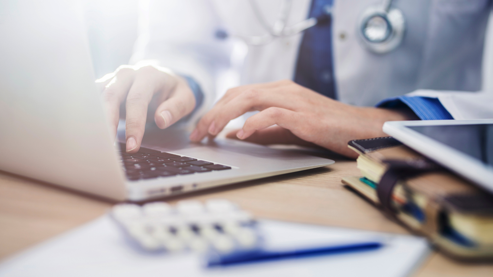 Person wearing a stethoscope typing on a laptop