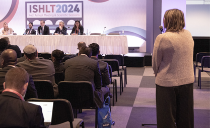 Woman in a tan sweater asks moderators a question during a session at ISHLT2024
